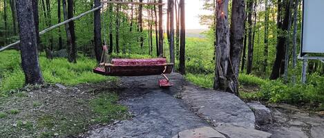 A rustic outdoor setting with a swing, a fire pit, and a stone pathway.