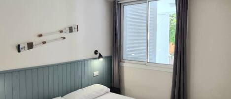 Un dormitorio con una cama, ventilador de techo, ventana con cortinas y una lámpara de pared.