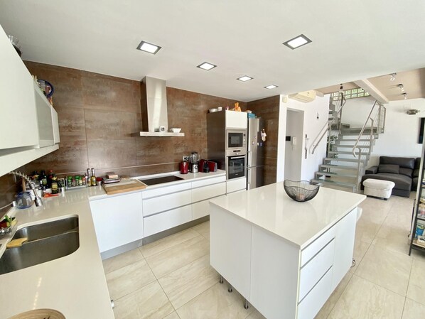 Una cocina moderna con armarios blancos, una isla central, electrodomésticos de acero inoxidable y un horno empotrado.