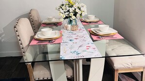 Een eettafel gedekt met witte borden, gouden bestek en een vaas met witte en gele bloemen.
