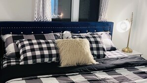 Een bed met een geruit beddegoed, een gestapeld hoofdbord en een bedlampje.