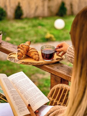 Eine Person liest ein Buch an einem Holztisch, auf dem ein Croissant und eine Tasse Tee stehen.