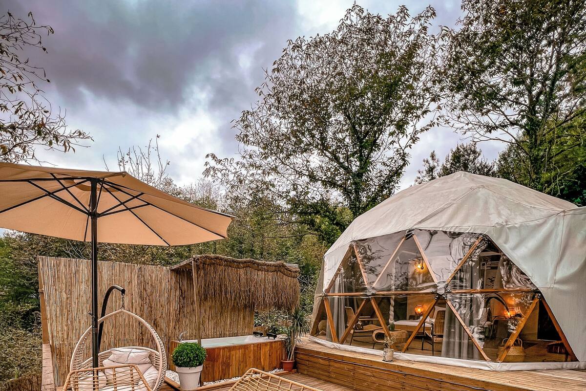 An outdoor patio with wicker furniture, a table set with food, a tent, and a wooden deck.