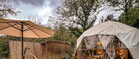 An outdoor patio with wicker furniture, a table set with food, a tent, and a wooden deck.