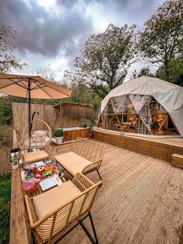 Eine Terrasse im Freien mit Korbmöbeln, einem Tisch gedeckt mit Speisen, einem Zelt und einem Holzboden.