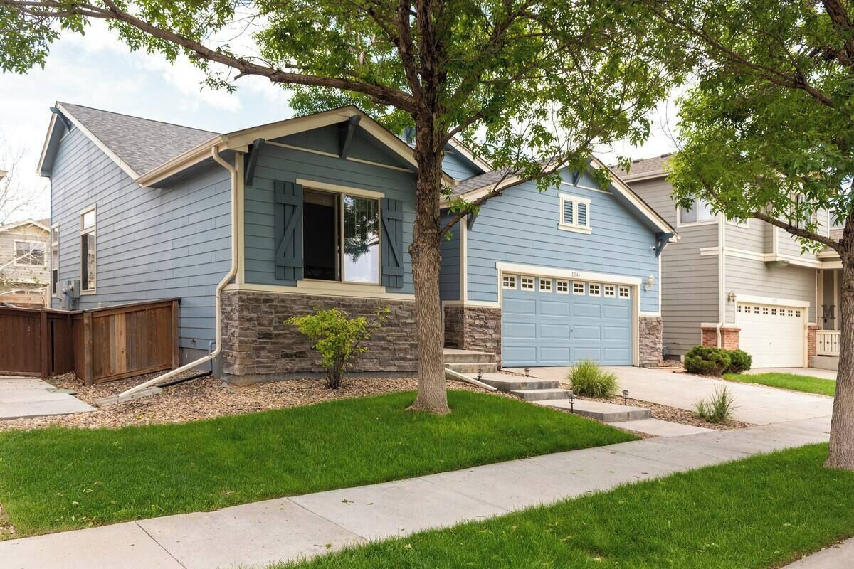 A two-story house with a stone foundation, a blue garage, and a well-maintained lawn.