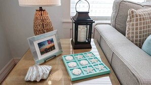 Une table basse en verre sur laquelle sont posés un tableau encadré, une lanterne et des biscuits en forme d’étoile de mer.