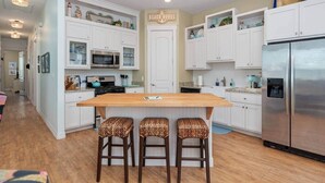 Une cuisine moderne avec des meubles blancs, un îlot central doté de tabourets, des appareils en acier inoxydable et une enseigne indiquant « Beach House ».