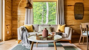 L’intérieur d’un chalet accueillant, avec un revêtement mural en bois, un canapé avec des coussins, une table basse et une fenêtre avec des rideaux.