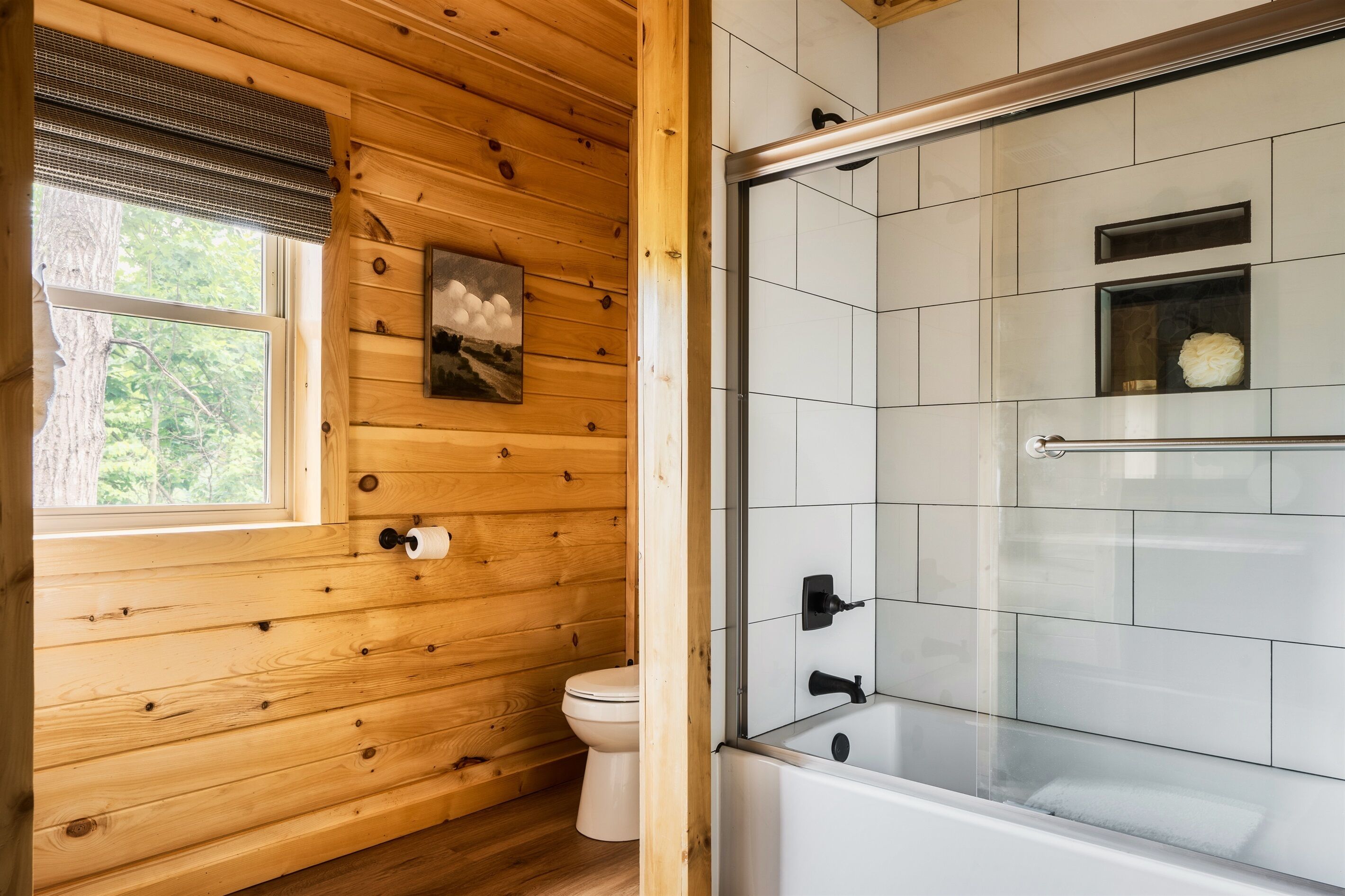 A wooden-paneled bathroom with a toilet, a glass-enclosed shower, and a white tiled wall.