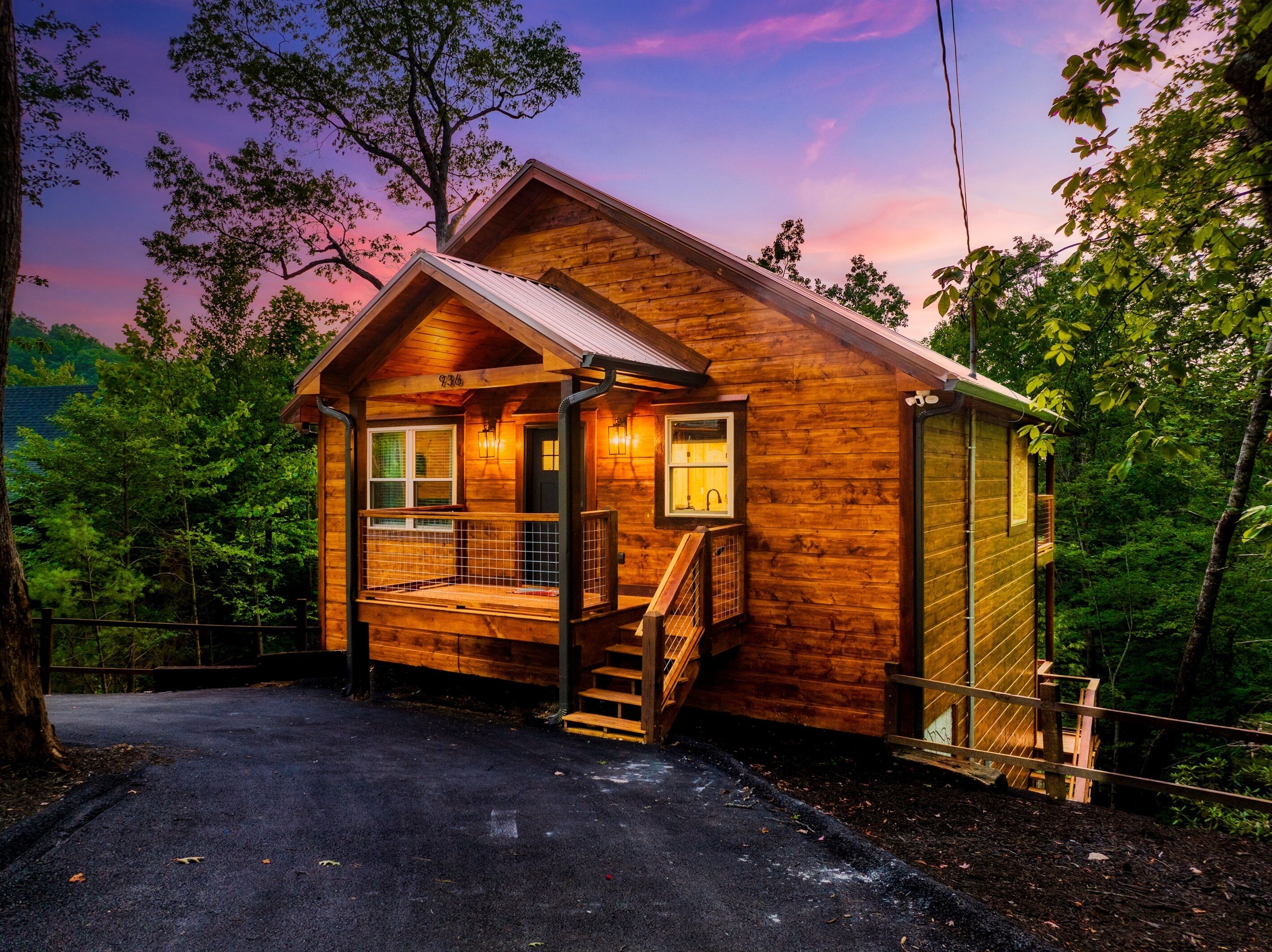 A wooden cabin with a porch, a staircase, and a view of the surrounding forest.