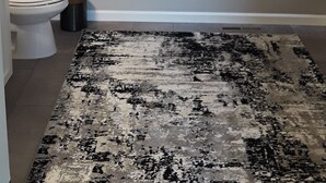 Et badeværelse med toilet, håndklæder på en håndklæderstang, en måtte og et gardin foran et vindue.