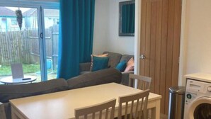 A compact living space with a dining table and chairs, a sofa, a washing machine, and a sliding glass door leading to a backyard. - Lovely 5-Bed House in Brighton (Brighton)