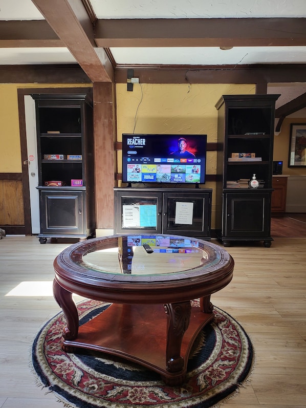 A living room with a television displaying a show, a round glass coffee table, and wooden bookshelves.