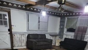 A room with wooden flooring, two sofas, a patterned rug, and a ceiling fan.
