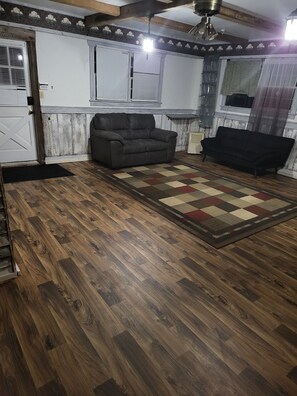 A room with wooden flooring, two sofas, a patterned rug, and a ceiling fan.