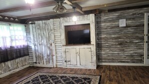 A rustic room with a wooden floor, a large rug, a ceiling fan, and a TV mounted on a wooden wall.