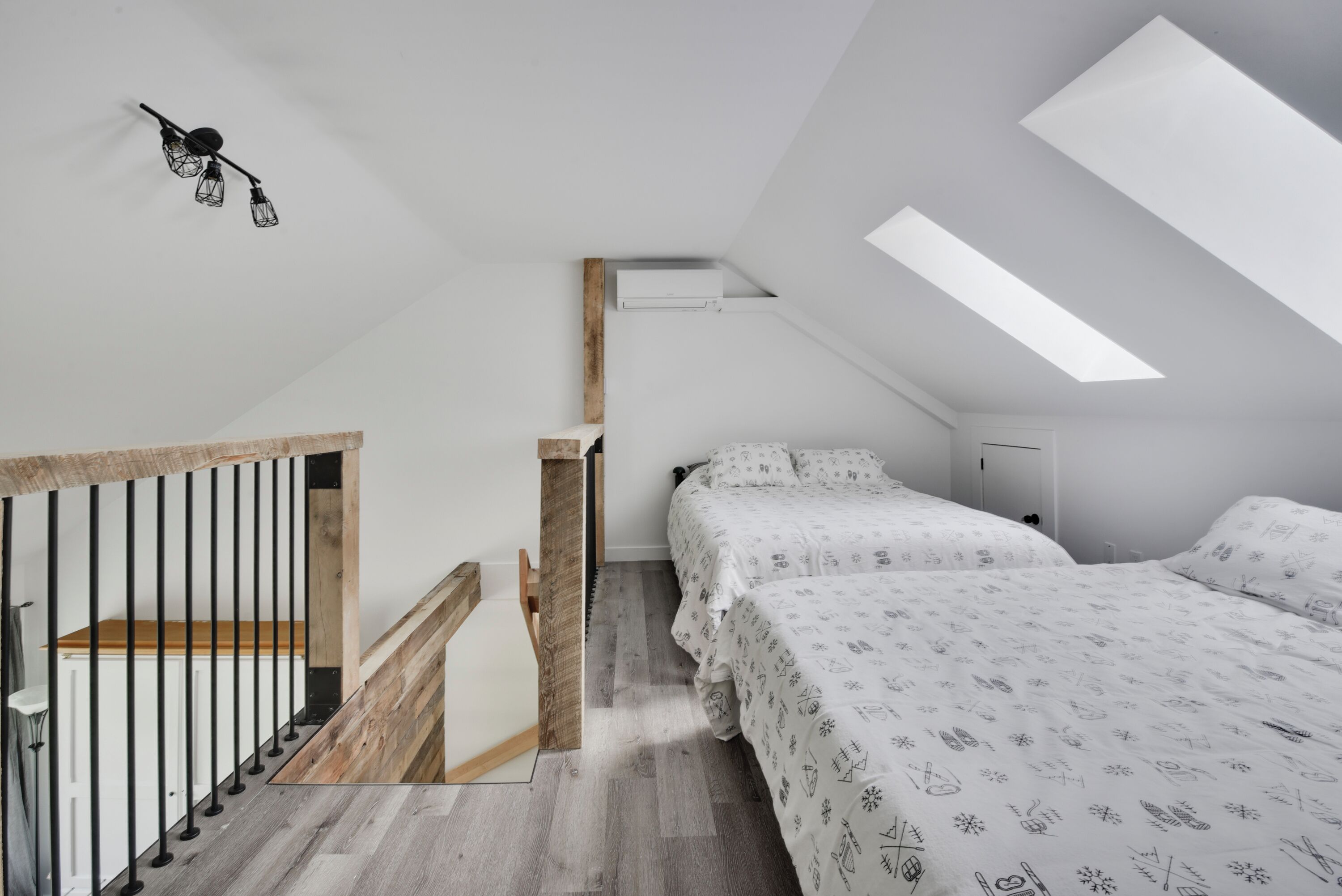 Une chambre moderne avec un plafond en pente, un escalier en bois, un lit avec une literie à motifs et un luminaire fixé au mur.