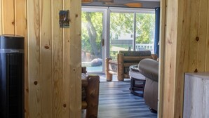 Ein Holzinnenraum mit Kamin, einer Couch und Blick durch eine Glastür.