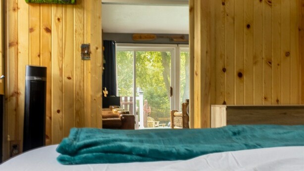 Ein Zimmer mit Holzwänden, einem Bett, einem Fernseher und Blick ins Freie.
