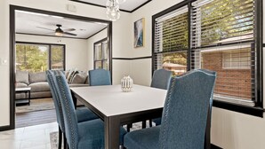 Un espace repas comprenant une table et des chaises, un ventilateur de plafond et de grandes fenêtres équipées de stores.