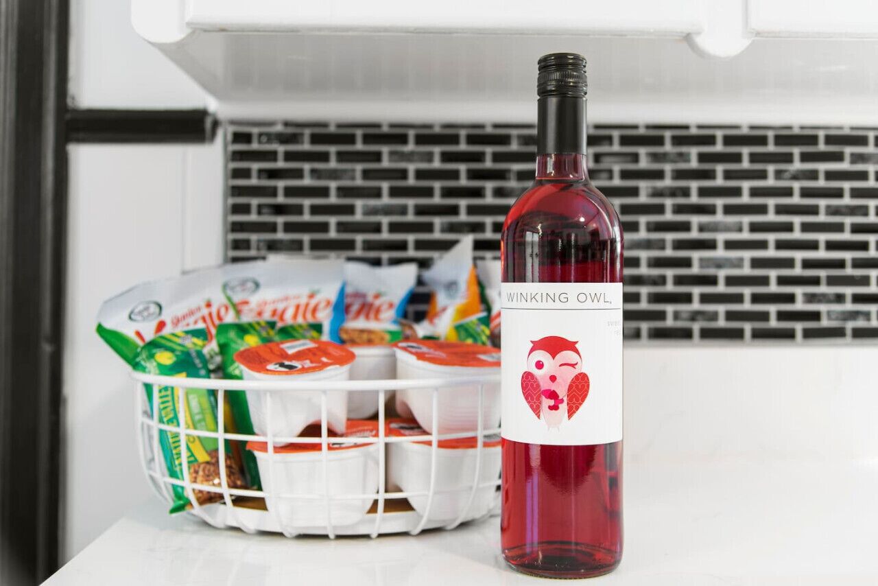 Een fles Winking Owl wijn naast een mand met verpakte snacks.