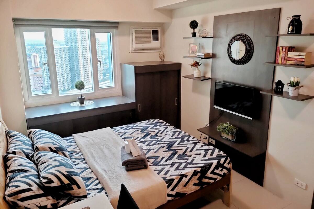 Ein modernes Schlafzimmer mit Bett, Fernseher und Fenster mit Blick auf die Stadt.