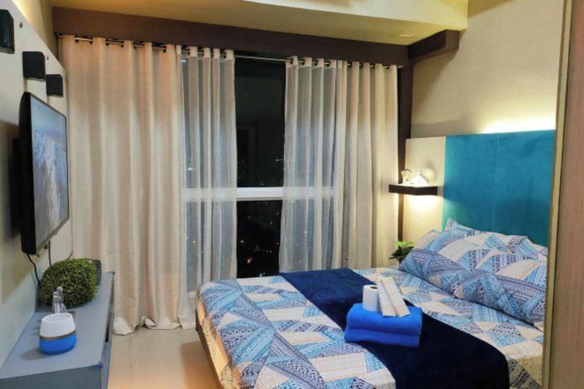 Een hotelkamer met een bed, gordijnen, een televisie, een nachtkastje en een bijzettafeltje.