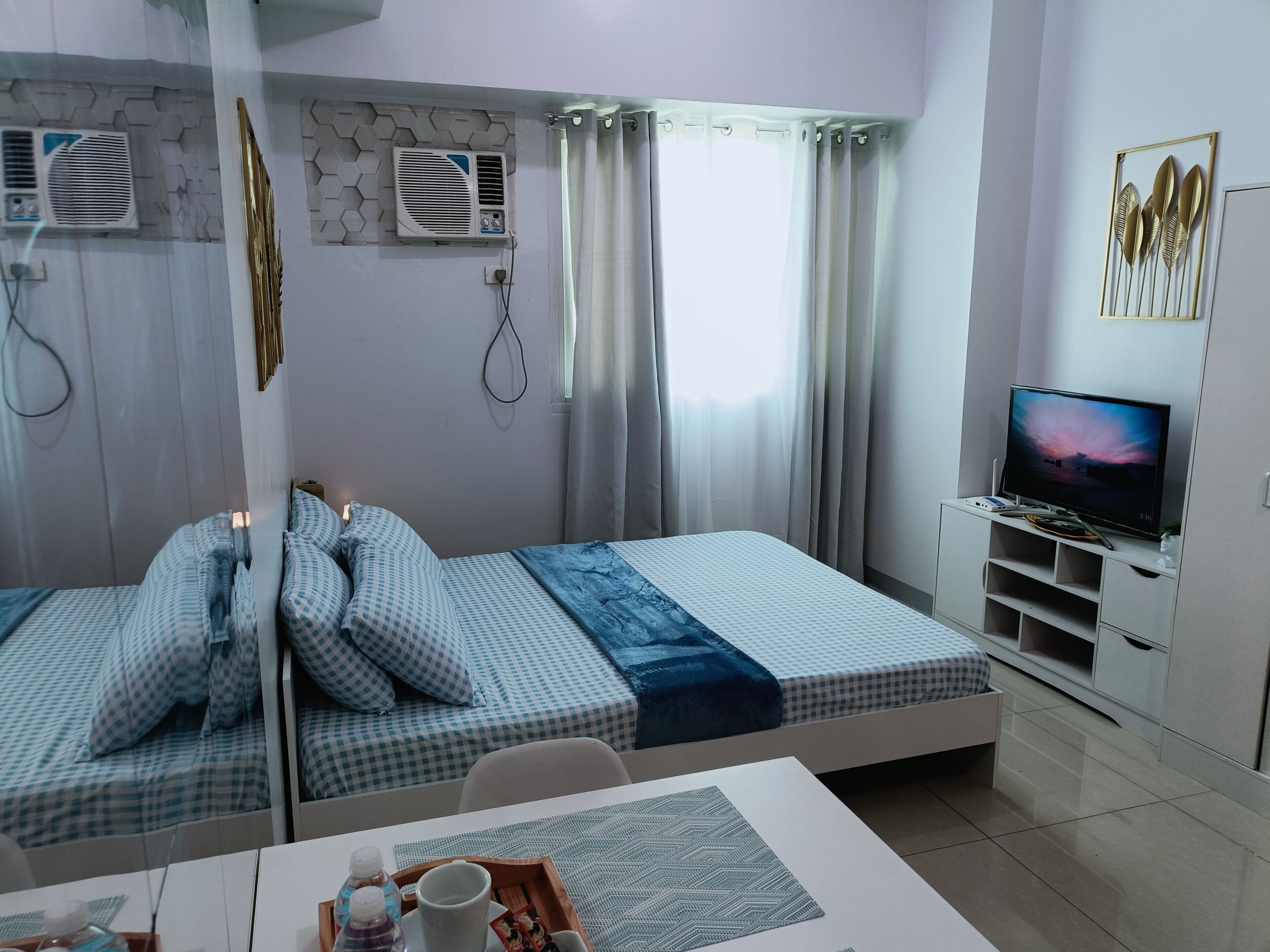 Ein Hotelzimmer mit zwei Betten, einem Fernseher, einem Schreibtisch und einem Vorhangfenster.
