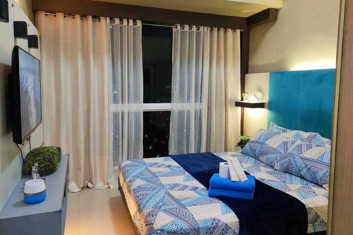 Ein modernes Hotelzimmer mit einem großen Bett, einem Nachttisch, einer kleinen Topfpflanze und einem Vorhangfenster.