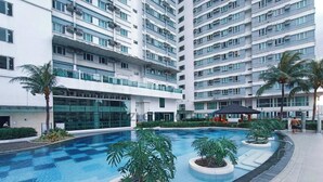Een modern appartementencomplex met een centraal gelegen zwembad, omringd door plantenbakken en palmbomen.