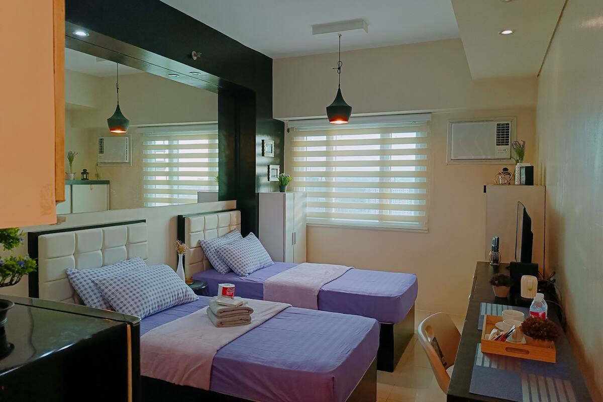 Ein Hotelzimmer mit zwei Betten, einem Schreibtisch, einem Stuhl, einem Spiegel und einem Fenster mit Jalousien.