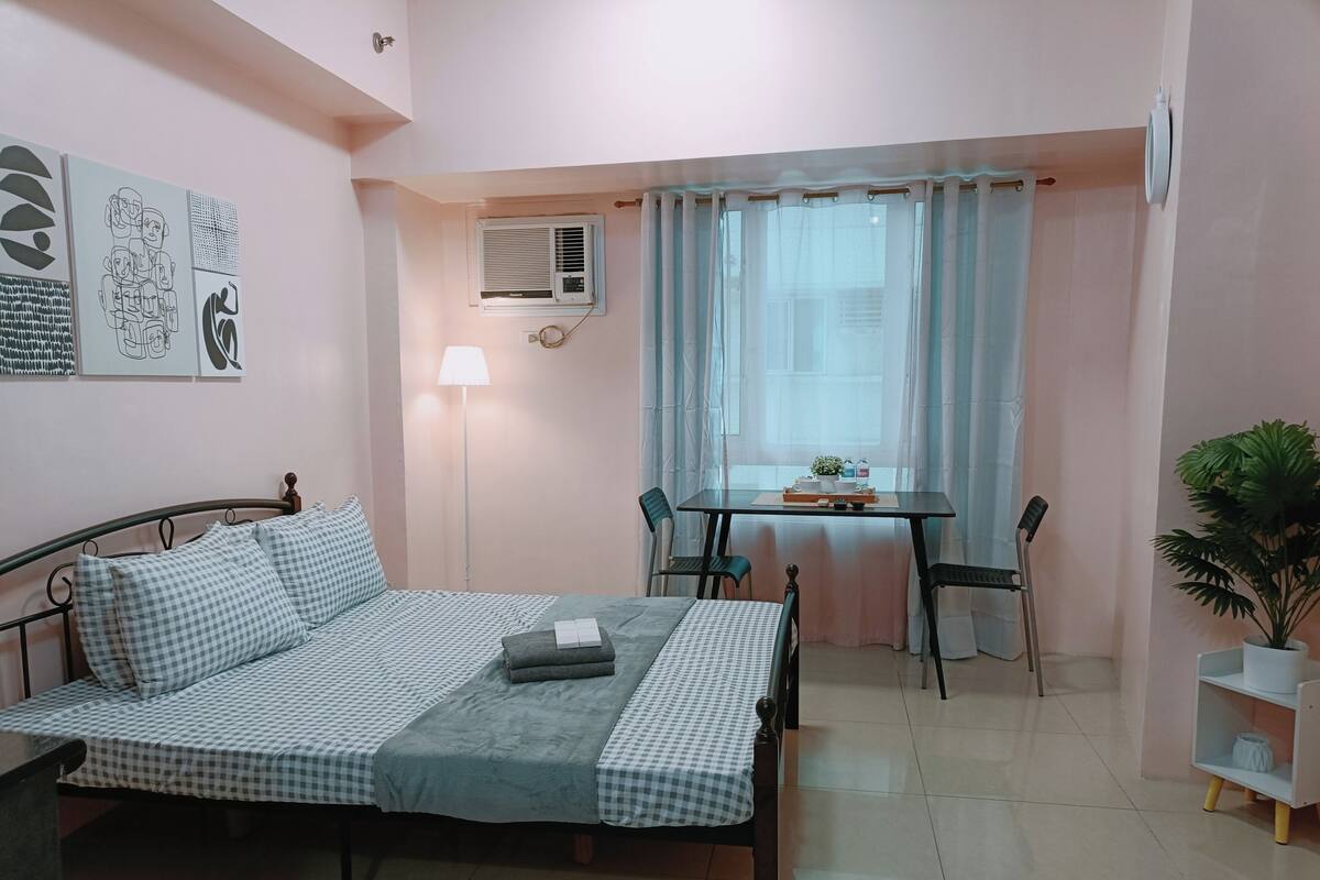 Ein Schlafzimmer mit einem Bett, einem Schreibtisch, einem Sessel, einer Lampe und einem Blumentopf.