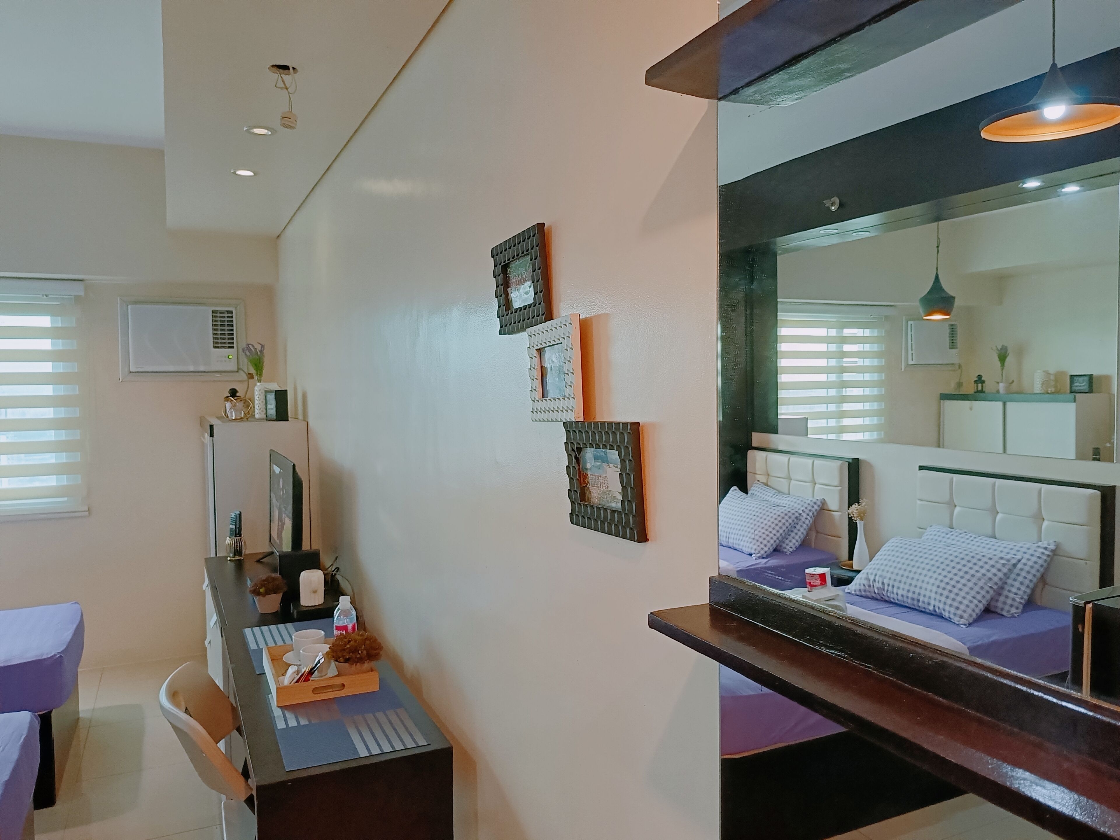 Une chambre à coucher moderne avec un grand lit, un bureau avec un ordinateur et un miroir qui reflète la pièce.