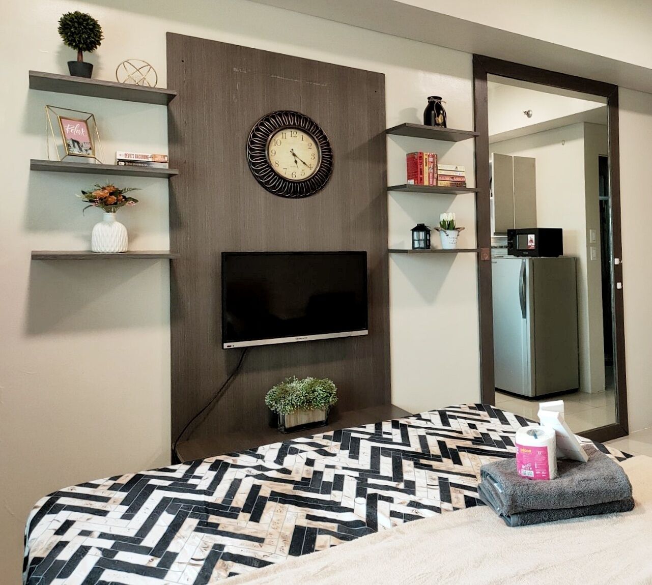 A modern bedroom with a TV mounted on the wall, a bed with a patterned bedspread, and a small potted plant on the nightstand.