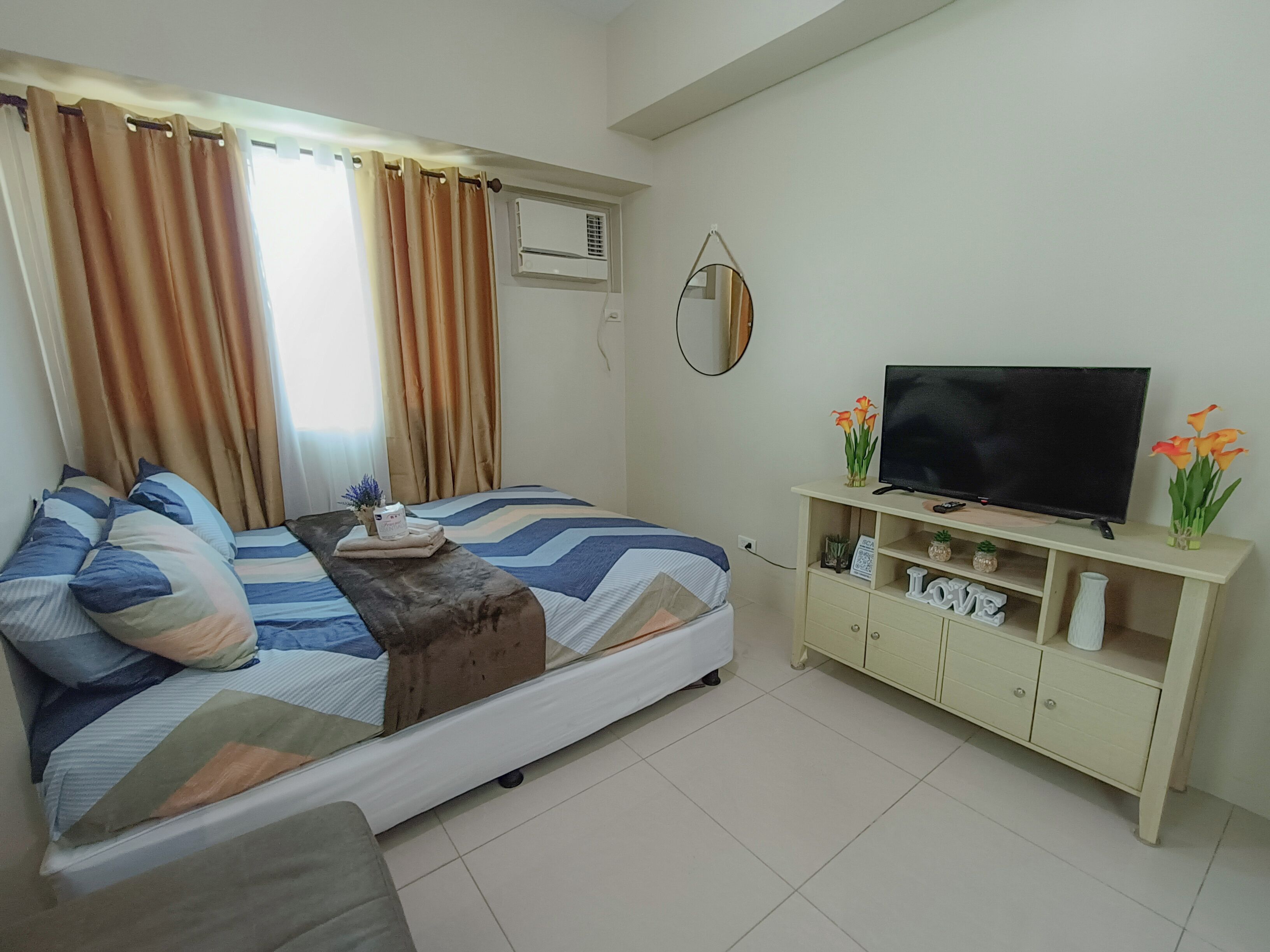 A bedroom with a bed, a TV, a dresser, and a window with curtains.