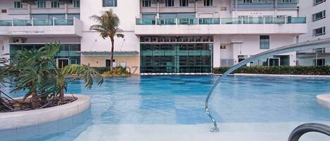A modern hotel with a swimming pool surrounded by palm trees and a glass building.