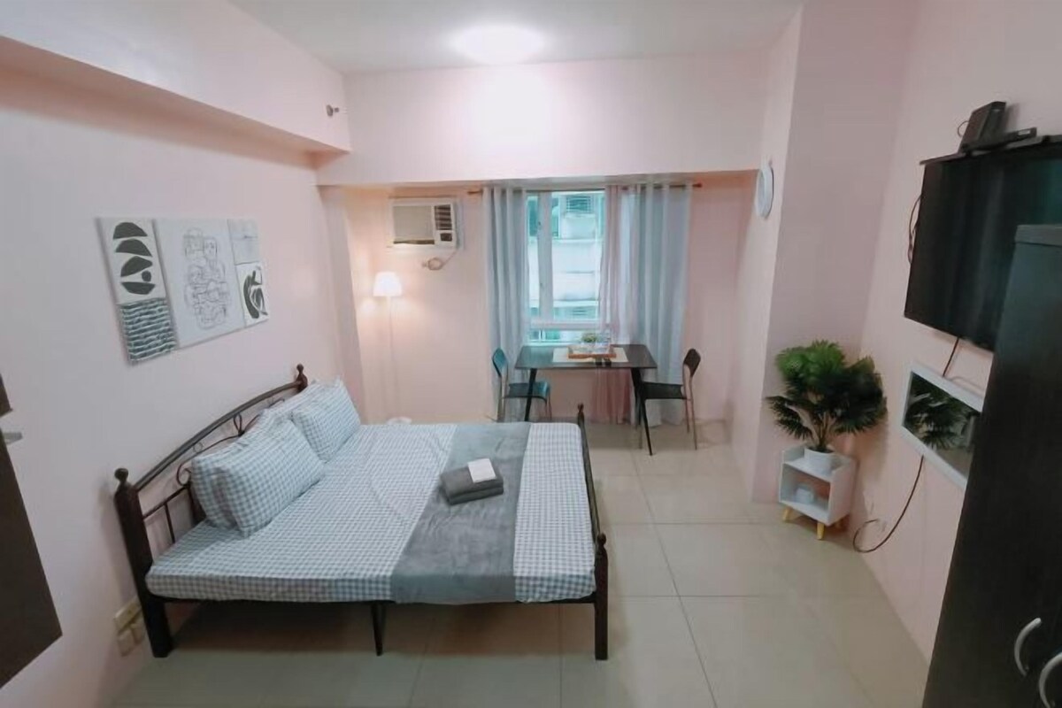 Une chambre à coucher comprenant un lit, un bureau, une chaise, un téléviseur et une fenêtre avec des rideaux.