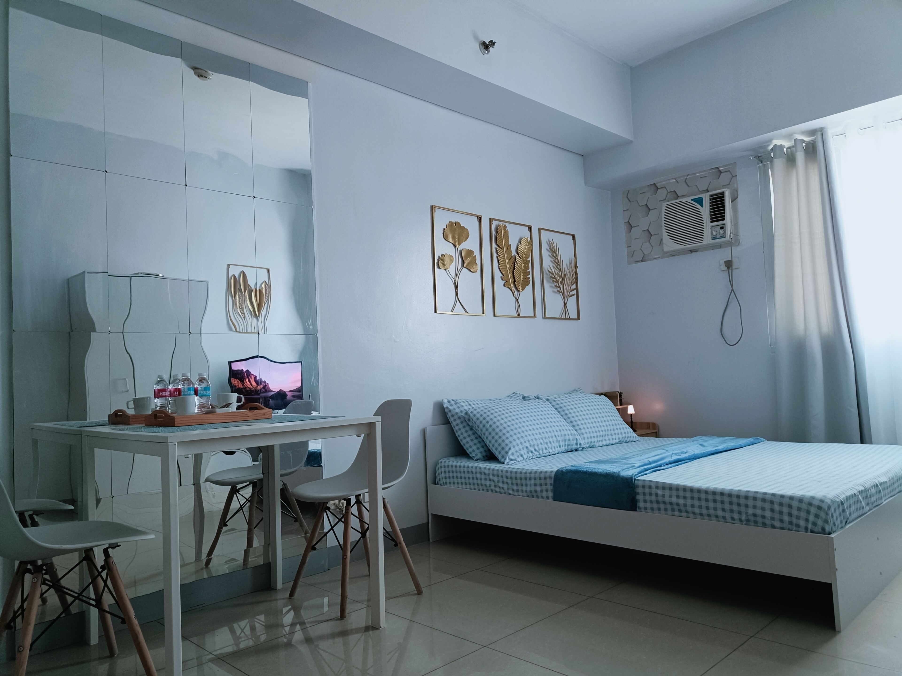 Un dormitorio moderno con cama, escritorio y silla. Hay cuadros enmarcados en la pared, una ventana con cortinas y un equipo de aire acondicionado instalado en la pared.