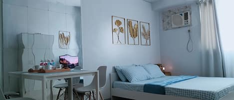 Un dormitorio moderno con cama, escritorio y silla. Hay cuadros enmarcados en la pared, una ventana con cortinas y un equipo de aire acondicionado instalado en la pared.