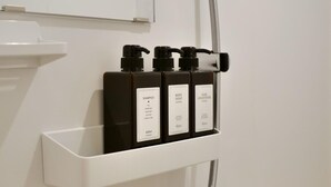 A bathroom with a white shelf holding three bottles of shampoo, body soap, and hair conditioner. - 2023 Open/Shinjuku Okubo/5min 2 JR/Premium Capsule (Shinjuku City)