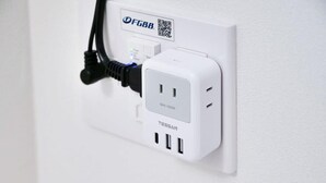 Un mur blanc avec une prise électrique blanche et un câble noir branché.