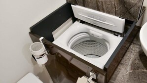 Une salle de bain moderne et compacte, dotée d’un appareil combiné lave-linge et sèche-linge intégré, de toilettes et d’un pare-feu en marbre.