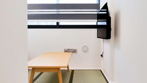Una habitación con una mesa de madera, un estante negro y una ventana con persianas.