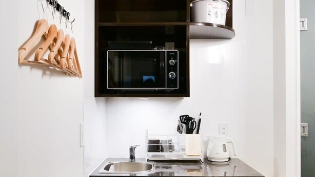 Una cocina moderna con encimera negra, microondas, hervidor y perchas de madera en la pared.
