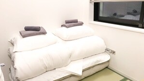 Una cama bien hecha con almohadas blancas y grises, un tapete a rayas verde y blanco, y una ventana con vistas al exterior.