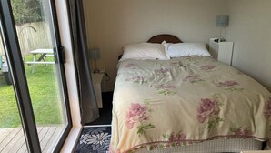 Une chambre à coucher comprenant un lit, une table de chevet, une lampe et donnant sur un patio avec une table et des chaises.