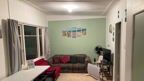 Un petit salon avec un canapé, une table et des chaises, un téléviseur et un ventilateur.