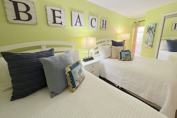 A room with two beds, a nightstand with a lamp, and a wall with the word "BEACH" spelled out in letters.