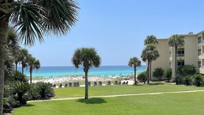Blick auf einen Strand mit Palmen, feinem Sand und einem Gebäude mit Balkonen.